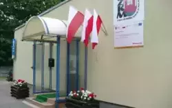 Zdjęcie przedstawia wejście do budynku Zakładu Komunikacji Miejskiej, budynek w kolorze żółtym, na ścianie logo ZKM, flagi polski zawieszone na ścianie budynku.