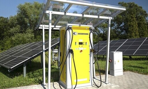 Żółta ładowarka do autonbusów elektrycznych a wokół niej panele fotowoltaiczne